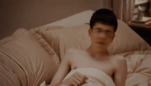 A Shirtless Man Is Laying In Bed With A Striped Comforter GIF