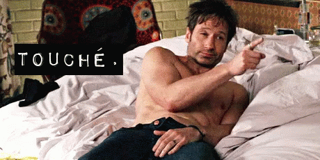 A Shirtless Man Is Laying On A Bed And Pointing At Himself With The Word Touche Above Him . GIF