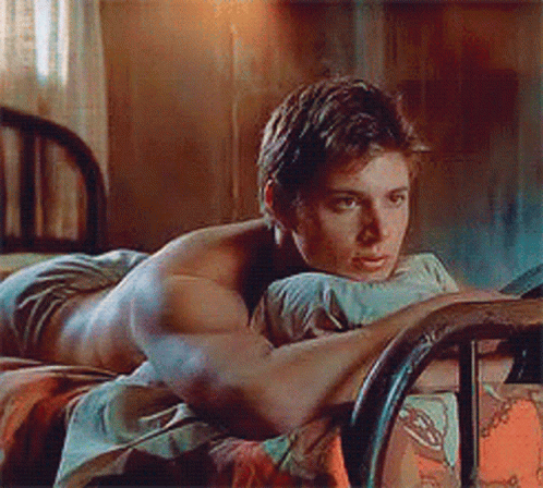A Shirtless Man Is Laying On A Bed With His Head On His Pillow GIF