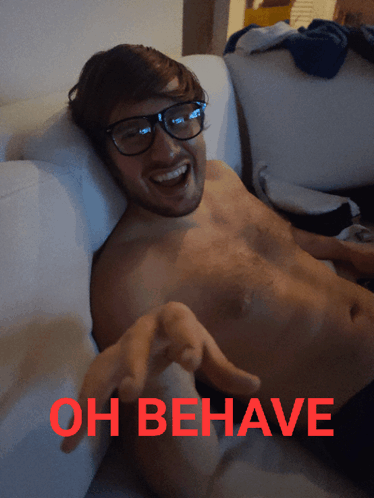 A Shirtless Man Is Laying On A Couch With The Words Oh Behave Written In Red GIF