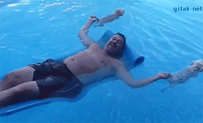 A Shirtless Man Is Laying On A Raft In A Swimming Pool With His Dog . GIF
