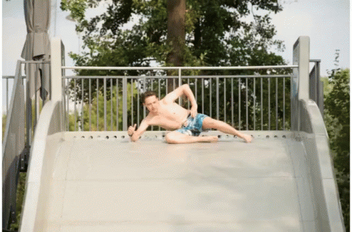 A Shirtless Man Is Laying On A Slide And Giving The Thumbs Up GIF