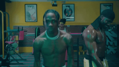 A Shirtless Man Is Lifting Weights In A Gym With Other Men GIF