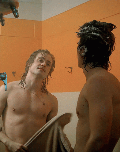 A Shirtless Man Is Looking At His Reflection In A Mirror GIF