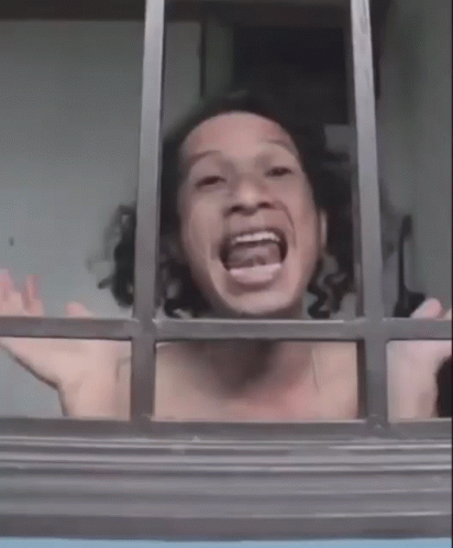 A Shirtless Man Is Looking Out Of A Window With His Mouth Open And His Arms Outstretched . GIF