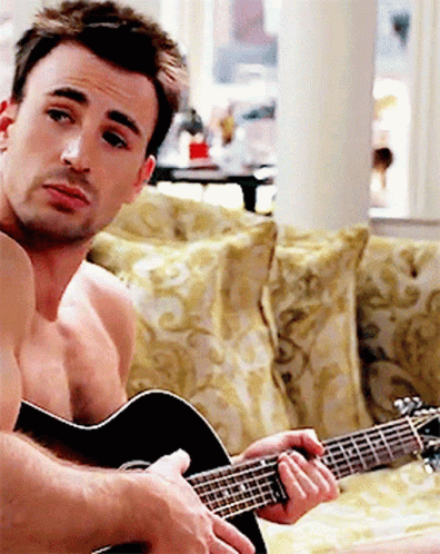 a shirtless man is playing an acoustic guitar on a couch