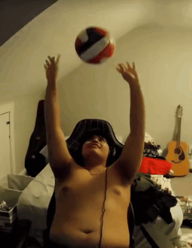 A Shirtless Man Is Playing With A Volleyball In A Bedroom GIF