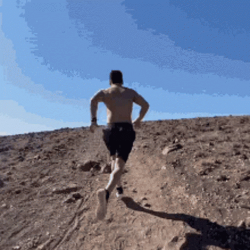 A Shirtless Man Is Running Up A Hill In The Desert GIF