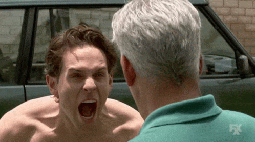 A Shirtless Man Is Screaming At Another Shirtless Man In Front Of A Car That Says Fx GIF