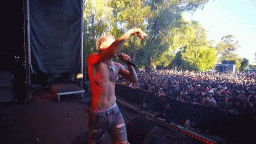 A Shirtless Man Is Singing Into A Microphone At A Concert GIF