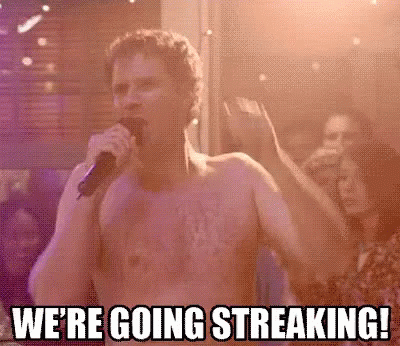 A Shirtless Man Is Singing Into A Microphone In Front Of A Crowd At A Party . GIF