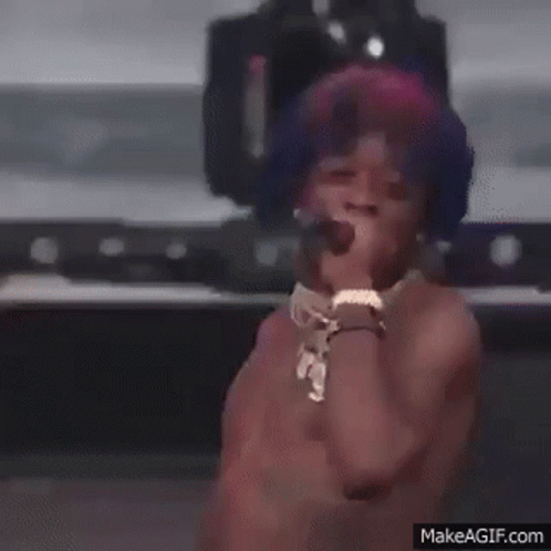 A Shirtless Man Is Singing Into A Microphone On A Stage . GIF