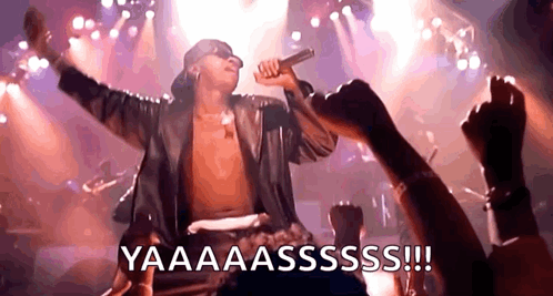 A Shirtless Man Is Singing Into A Microphone On A Stage While A Crowd Watches . GIF