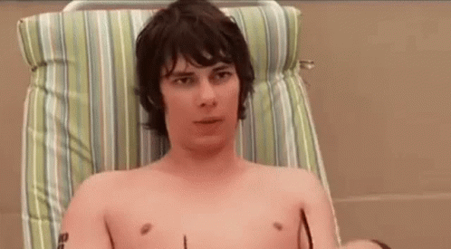 A Shirtless Man Is Sitting In A Chair With Sunglasses On . GIF