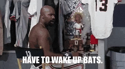 A Shirtless Man Is Sitting In A Chair With The Words Have To Wake Up Bats . GIF