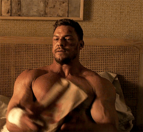A Shirtless Man Is Sitting On A Bed With His Eyes Closed GIF