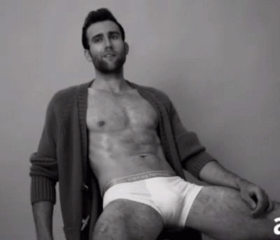 A Shirtless Man Is Sitting On A Chair Wearing White Underwear And A Cardigan . GIF