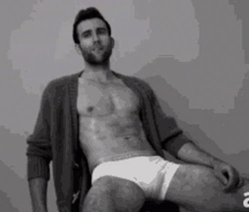 A Shirtless Man Is Sitting On A Chair With His Legs Crossed . GIF