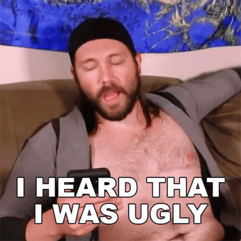 A Shirtless Man Is Sitting On A Couch Holding A Cell Phone And Says I Heard That I Was Ugly GIF