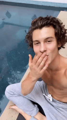 A Shirtless Man Is Sitting On The Edge Of A Pool Covering His Mouth With His Hand . GIF