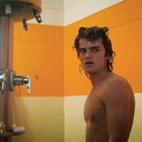 A Shirtless Man Is Standing In A Bathroom Next To A Shower Head GIF