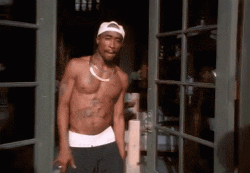 A Shirtless Man Is Standing In A Doorway Wearing A White Hat GIF