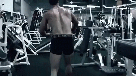 A Shirtless Man Is Standing In A Gym With A Bunch Of Exercise Equipment . GIF