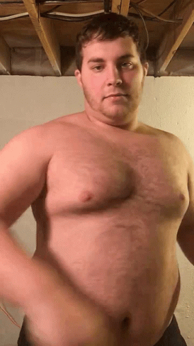 A Shirtless Man Is Standing In A Room With A Large Belly . GIF