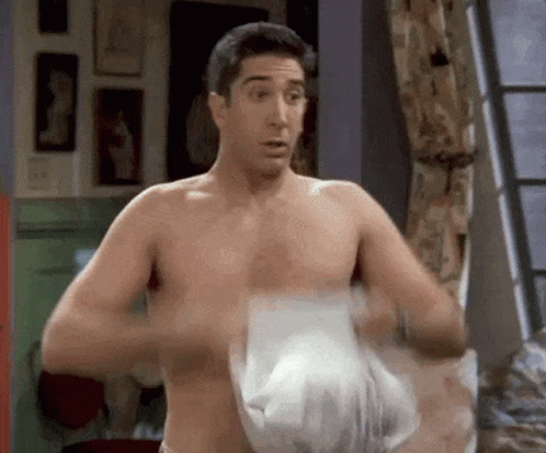A Shirtless Man Is Standing In A Room With A Towel Around His Waist . GIF