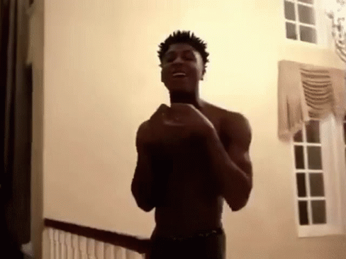A Shirtless Man Is Standing In A Room With His Hands In The Air . GIF