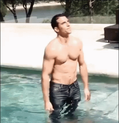 A Shirtless Man Is Standing In A Swimming Pool Wearing Wet Jeans . GIF
