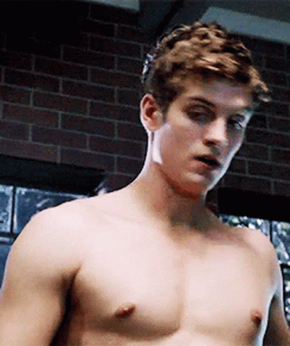 A Shirtless Man Is Standing In Front Of A Brick Wall In A Room . GIF