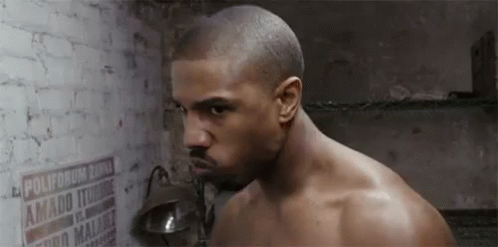A Shirtless Man Is Standing In Front Of A Brick Wall With A Lamp . GIF