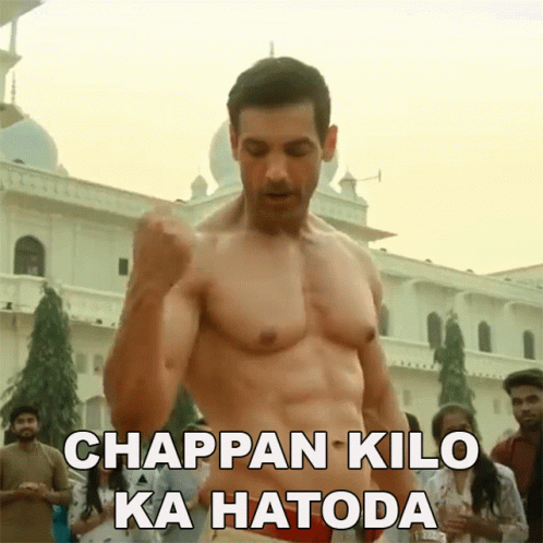 A Shirtless Man Is Standing In Front Of A Building With The Words Chappan Kilo Ka Hatoda Above Him GIF