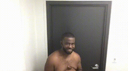 A Shirtless Man Is Standing In Front Of A Door With His Hands On His Chest . GIF