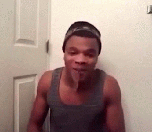 A Shirtless Man Is Standing In Front Of A Door With His Tongue Sticking Out . GIF