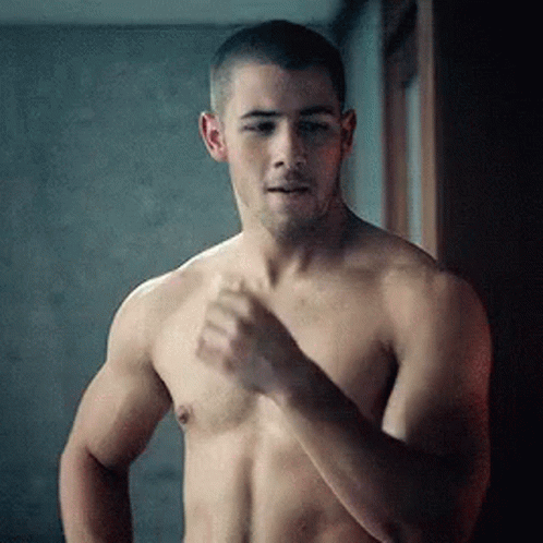 A Shirtless Man Is Standing In Front Of A Mirror Looking At Himself . GIF