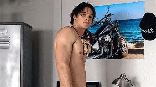 A Shirtless Man Is Standing In Front Of A Motorcycle Poster On A Wall . GIF