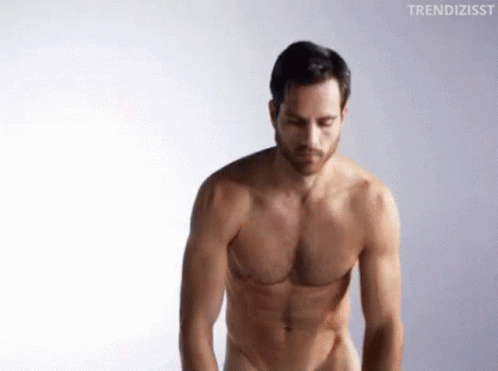 A Shirtless Man Is Standing In Front Of A White Background And Looking Down . GIF