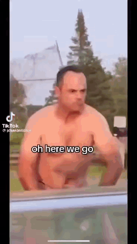 A Shirtless Man Is Standing In Front Of A Window With The Words `` Oh Here We Go '' Written On The Screen . GIF