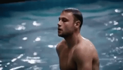 A Shirtless Man Is Standing In The Water With His Eyes Closed . GIF