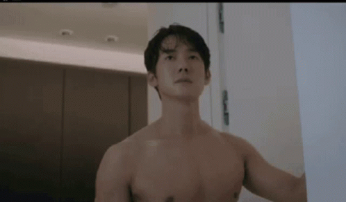 A Shirtless Man Is Standing Next To A Door In A Bathroom . GIF
