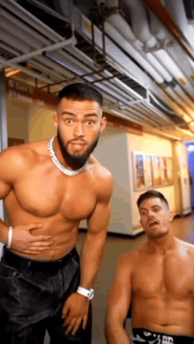 a shirtless man is standing next to a shirtless man in a hallway .