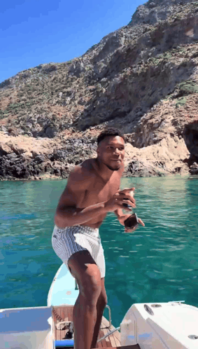 A Shirtless Man Is Standing On A Boat In The Ocean GIF