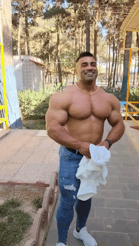 A Shirtless Man Is Standing On A Sidewalk Holding A Towel In His Hand . GIF