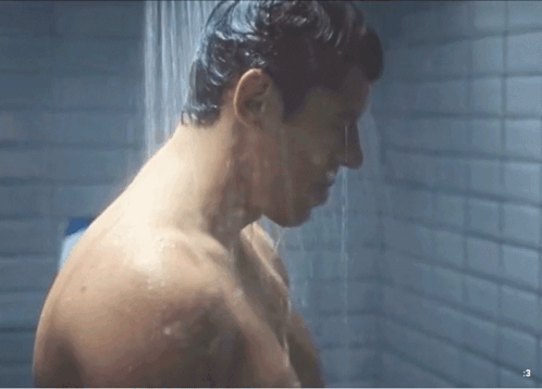 a shirtless man is taking a shower in a bathroom with a shower head .