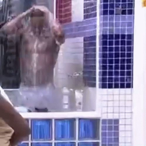 A Shirtless Man Is Taking A Shower In A Bathroom With Blue And White Tiles . GIF