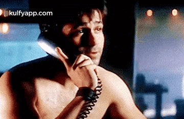 A Shirtless Man Is Talking On A Phone Without A Shirt On . GIF