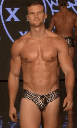 A Shirtless Man Is Walking Down A Runway In Front Of A Large X GIF