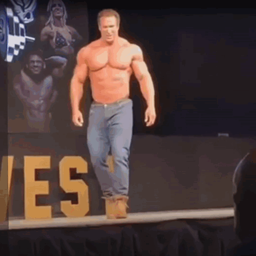 A Shirtless Man Is Walking Down A Stage With A Sign That Says Yes In The Background GIF
